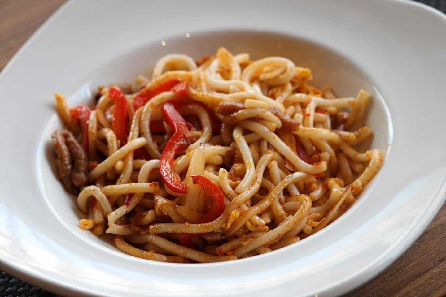 Piatto di noodles saltati in padella con cucchiaio e forchetta su una tovaglietta, con salsa per intingere lì vicino