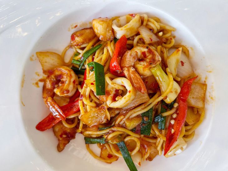 Spaghetti di mare saltati in padella con peperoncini rossi e verdure, serviti su un piatto bianco