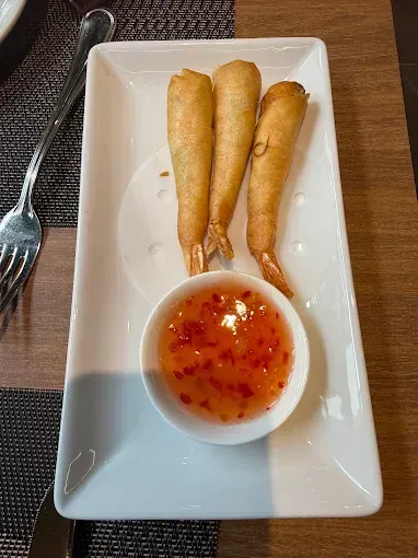 Tre involtini primavera fritti con salsa agrodolce al peperoncino, serviti su un piatto rettangolare bianco.