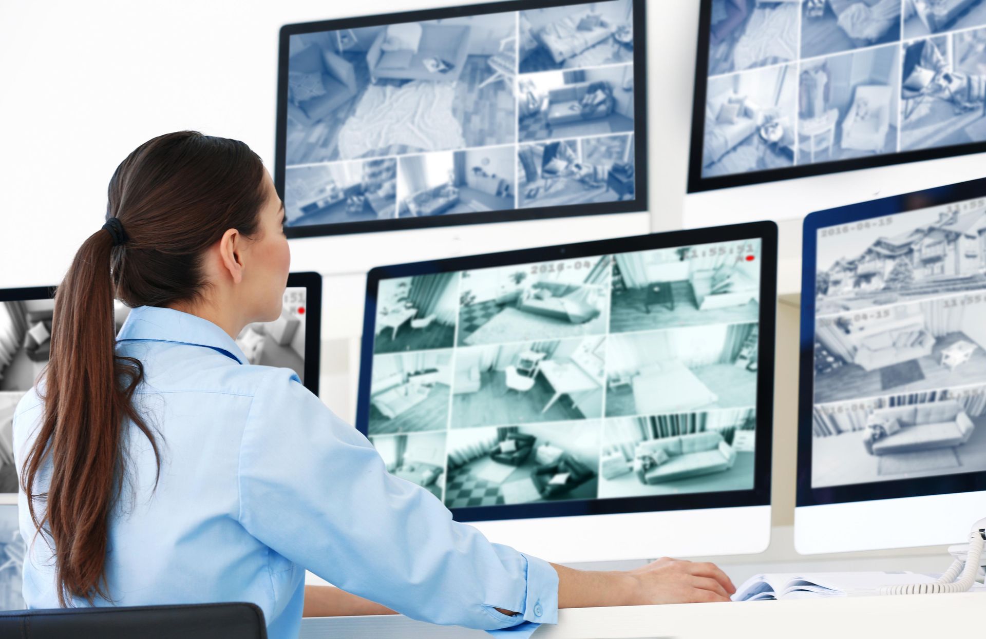 Woman monitoring security cameras in a control room. Multiple screens display live camera feeds.
