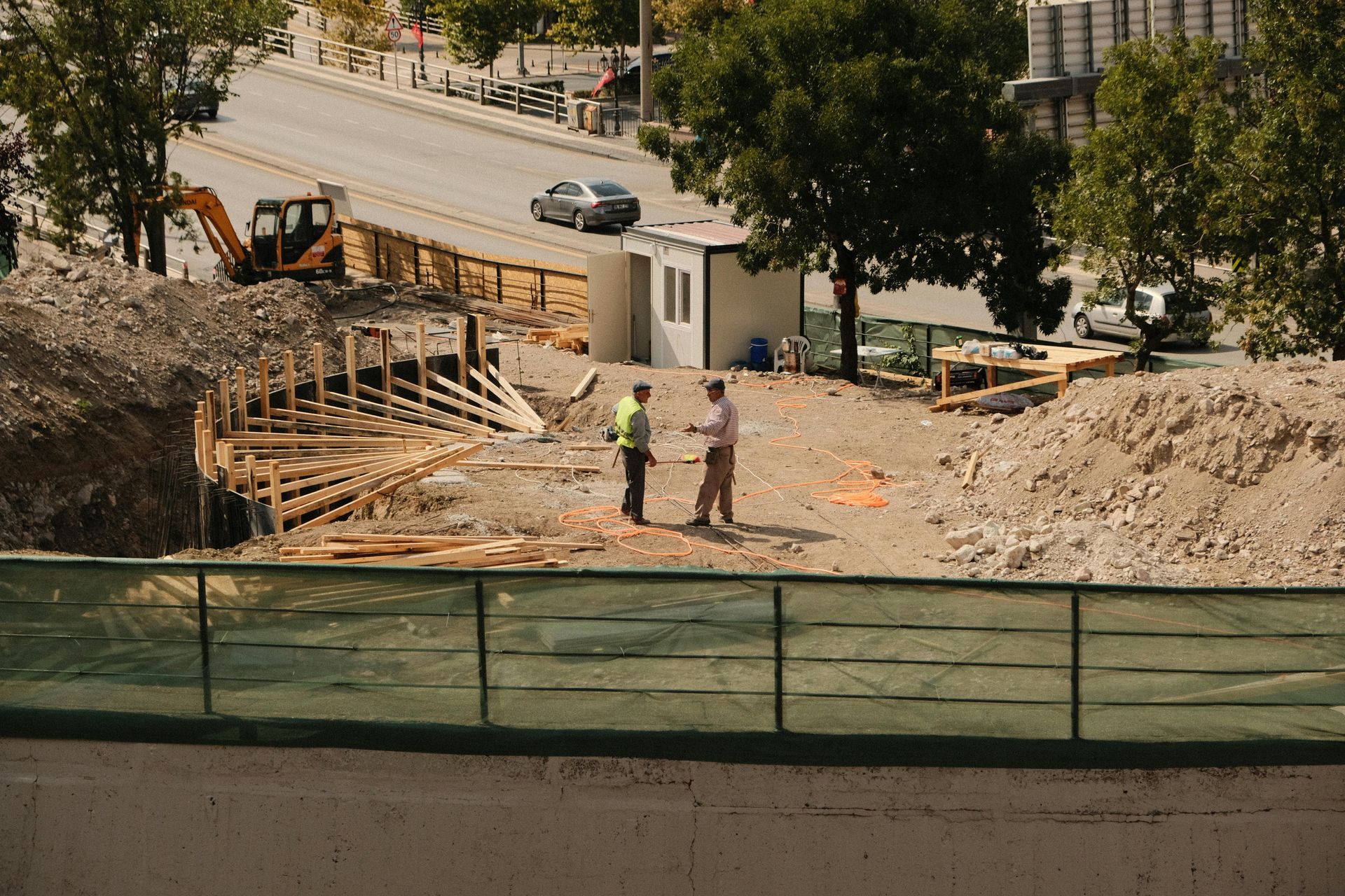 Two men are standing on a construction site next to a fence.
