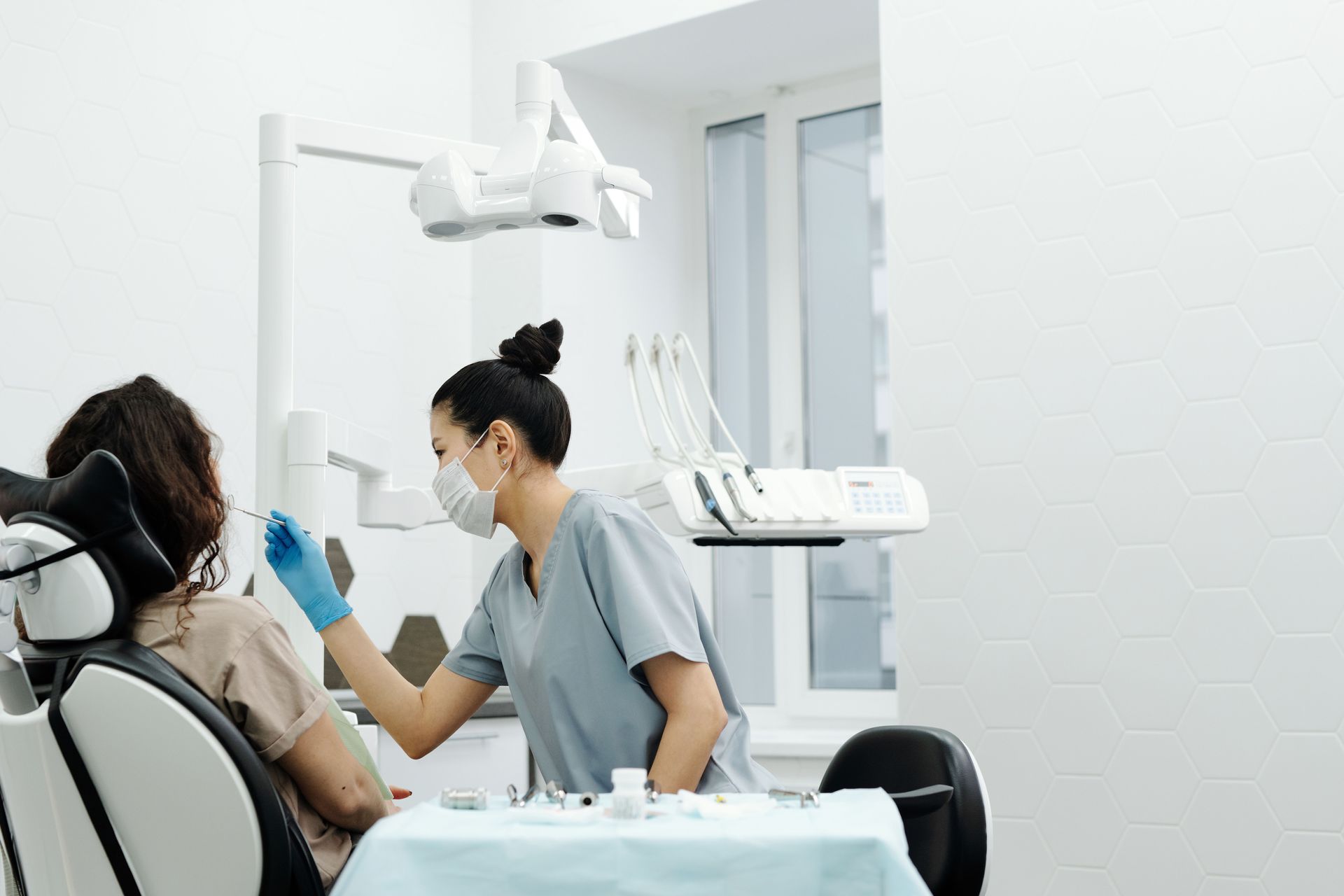 Dentist examining a patient in a bright dental clinic, with overhead light and equipment visible