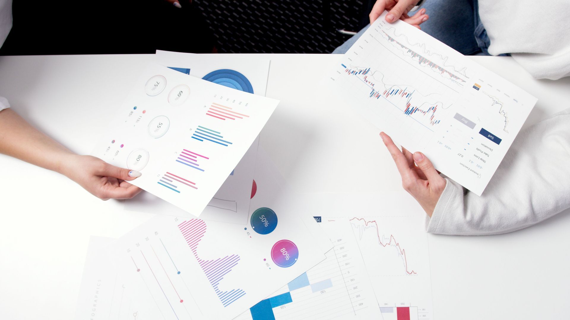 Two people sitting at a table with financial documents, comparing results