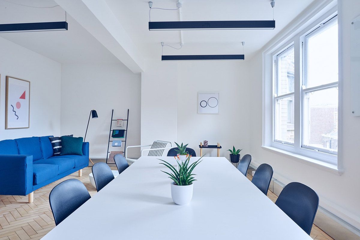 A conference room with a long white table and chairs and a blue couch.