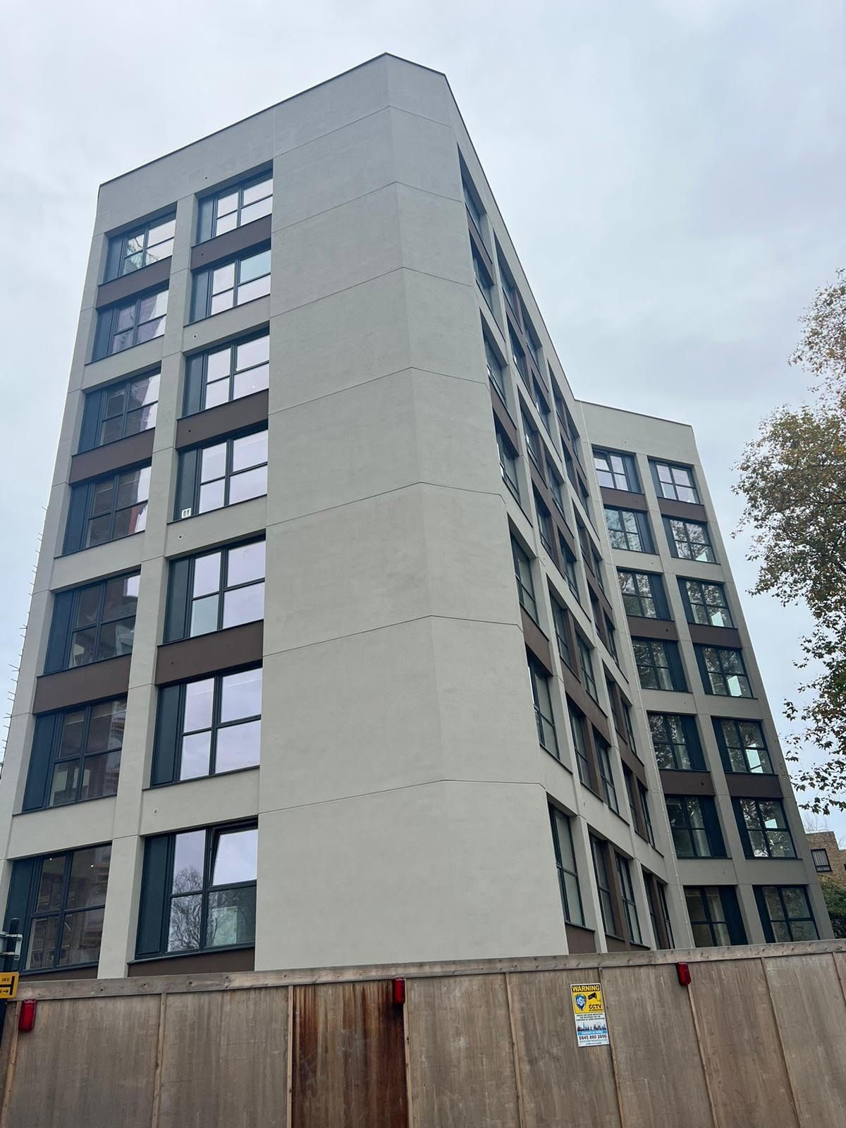 A large building with a lot of windows is behind a wooden fence.