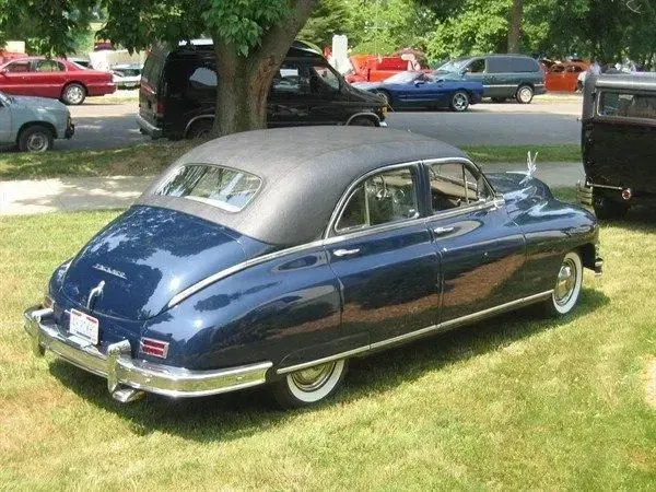 Blue vintage Packard sedan with black roof, parked on grass.