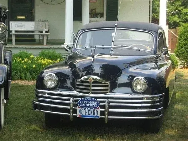 Dark blue vintage Packard car parked on grass, in front of a house.