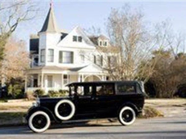 Black vintage car parked in front of a white Victorian house.