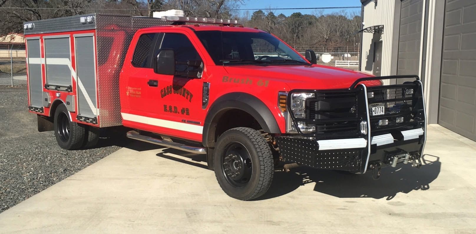 Red utility pickup truck with a utility bed parked on a driveway in bright daylight