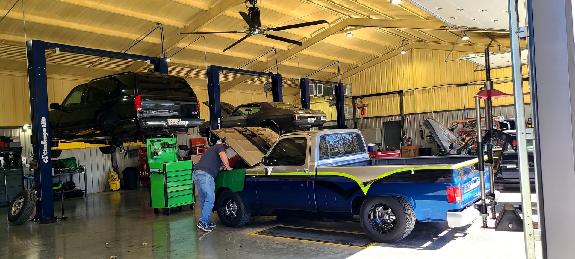 Auto repair shop with two classic cars, one blue and one black, and a mechanic working nearby