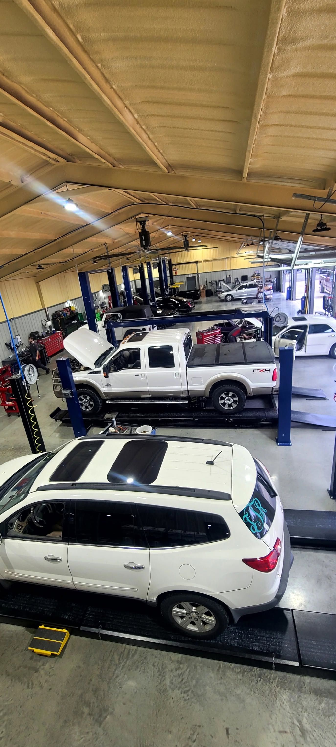 Several vehicles in a covered auto service bay with lifts and equipment.