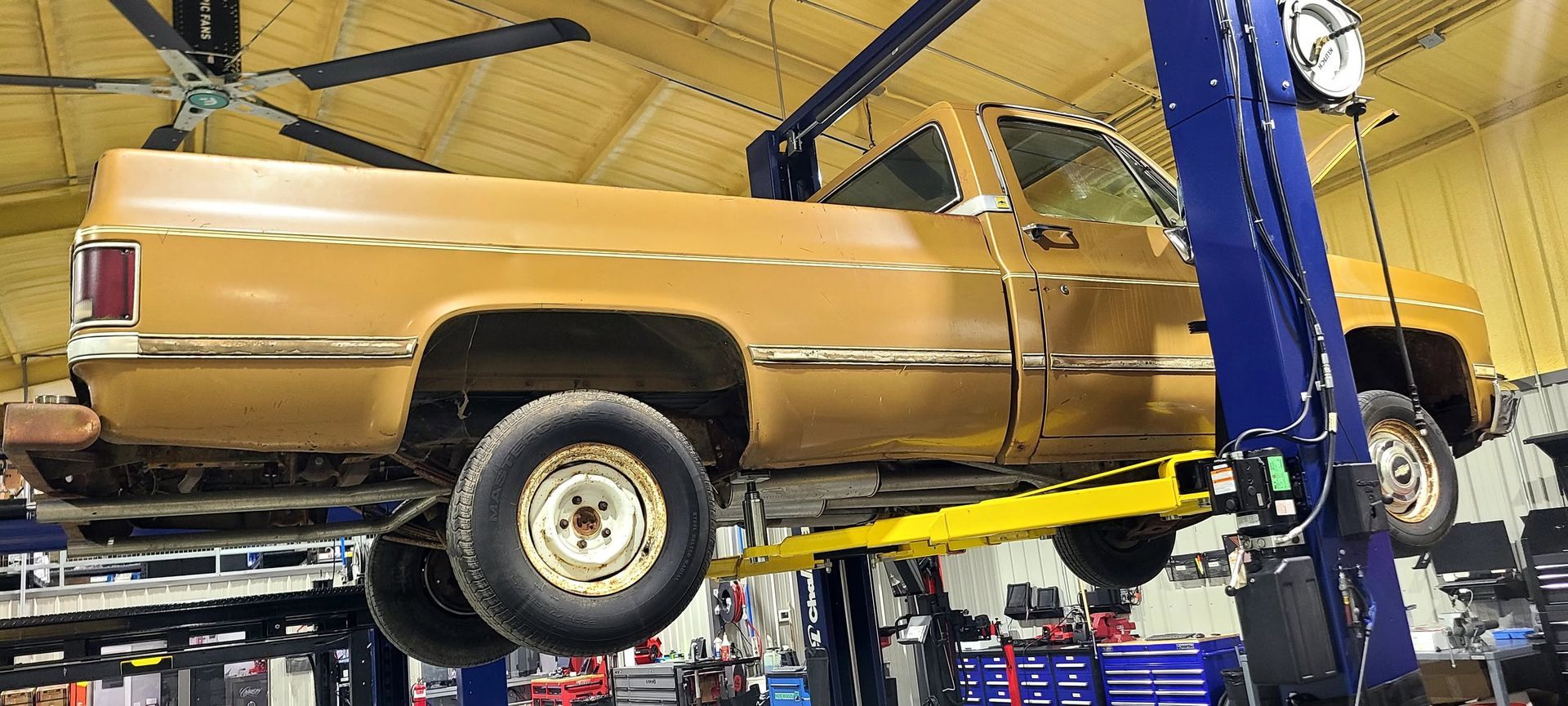 Brown pickup truck on a car lift in an auto repair garage, side view with raised rear wheel