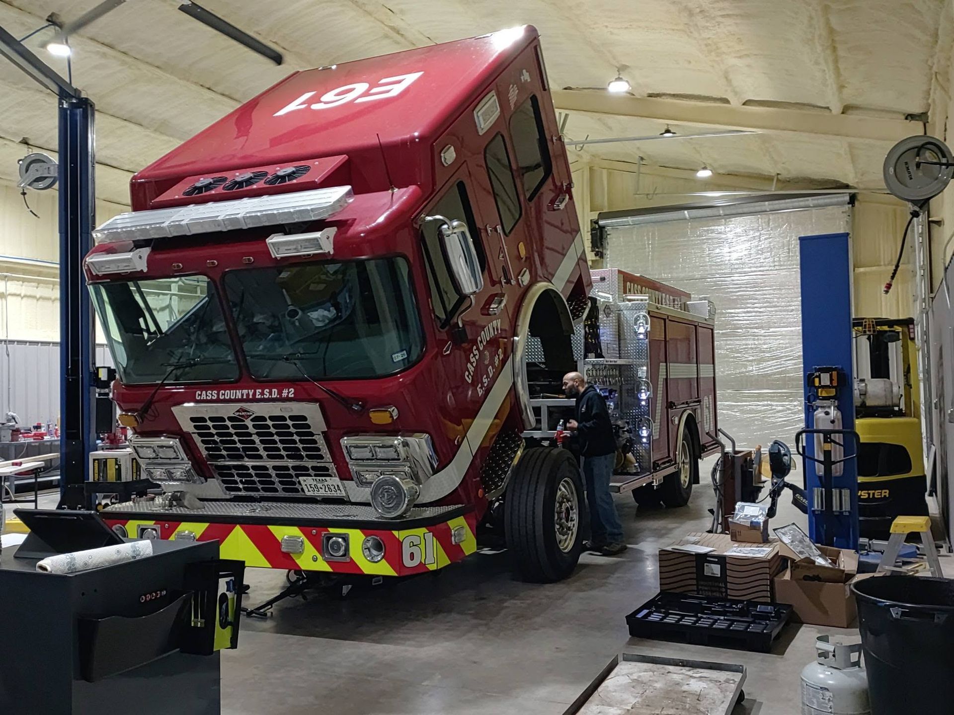Tilted red truck in an auto repair bay, with mechanics working underneath it.