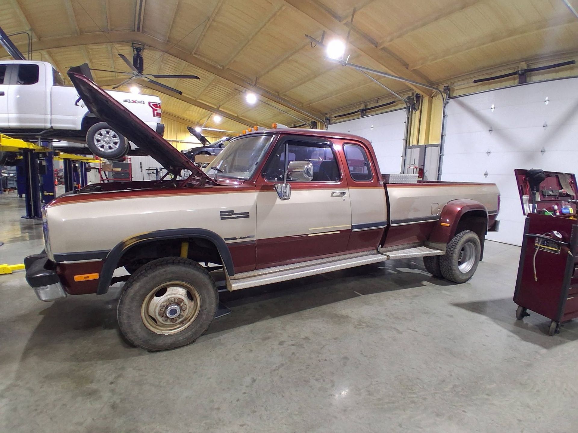 Two-tone pickup truck in a garage with hood open, showing the engine bay.