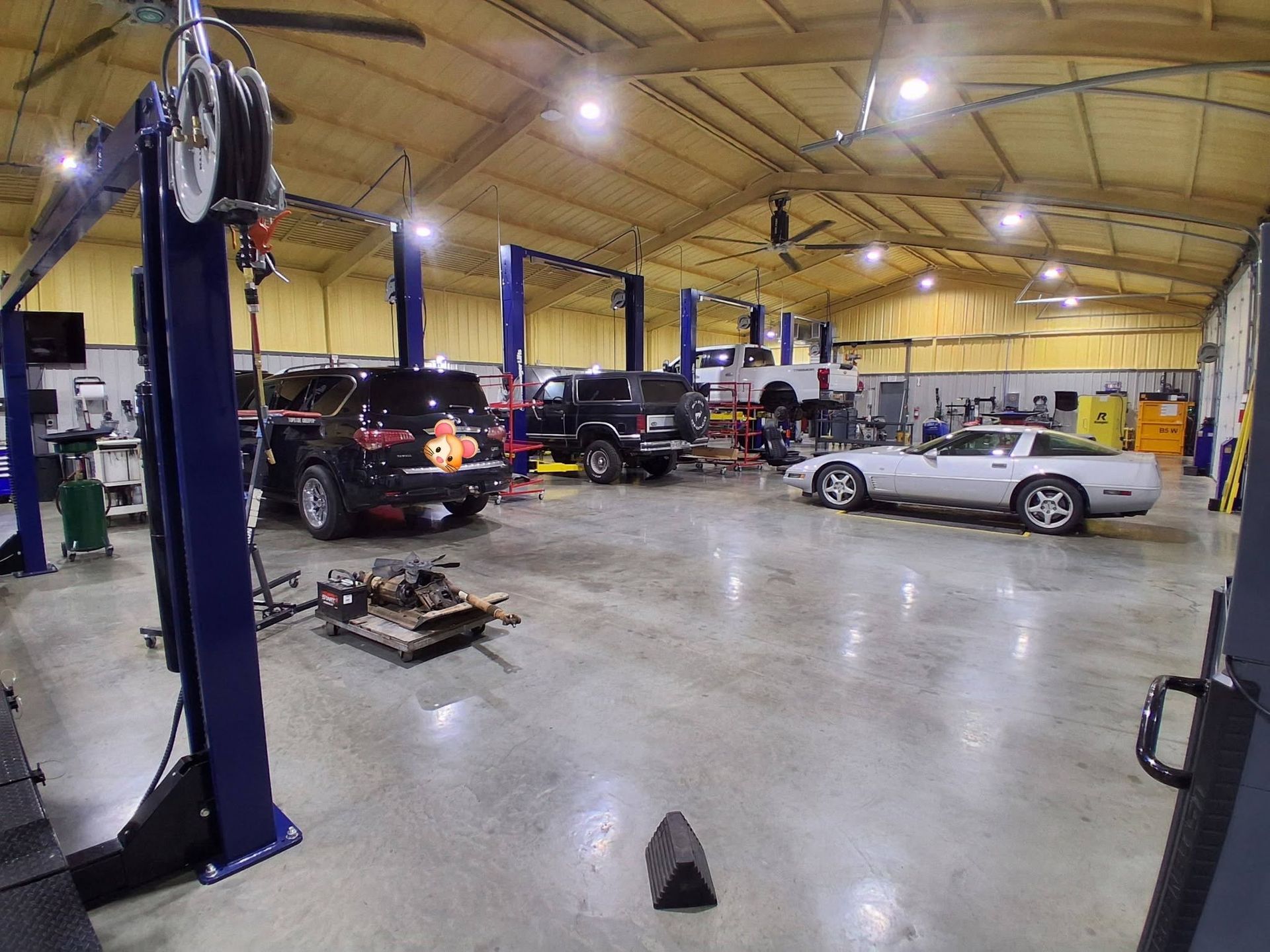 Car repair shop with several cars on lifts and parked under bright overhead lights
