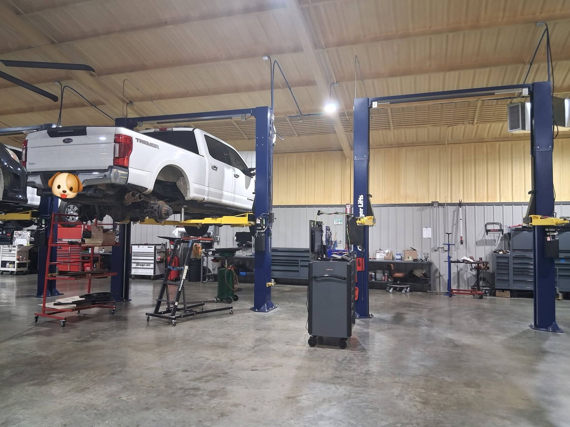 White pickup truck raised on a lift inside an auto repair shop with blue hydraulic posts