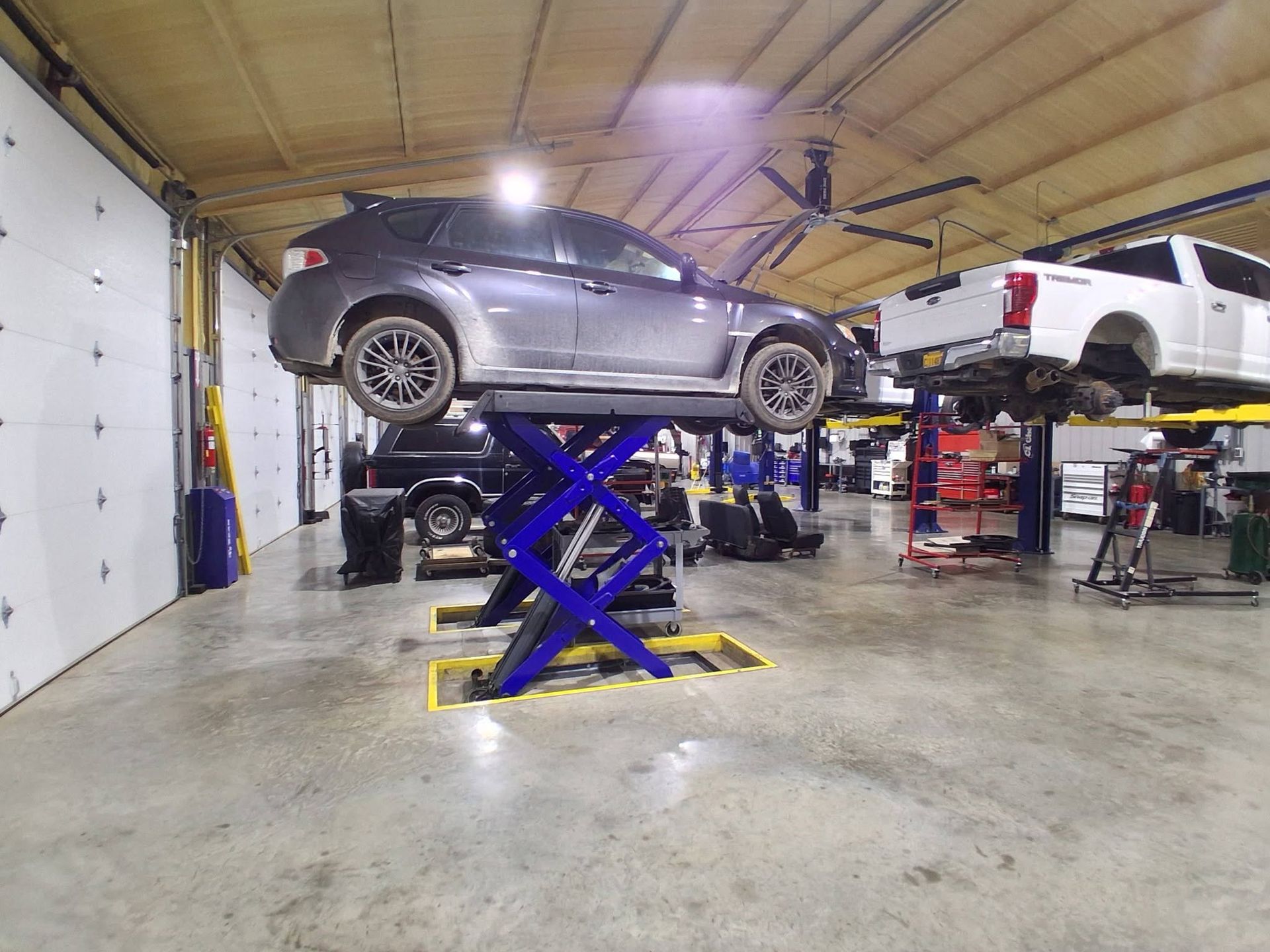 Two cars on hydraulic lifts inside an auto repair shop with a concrete floor and open garage door