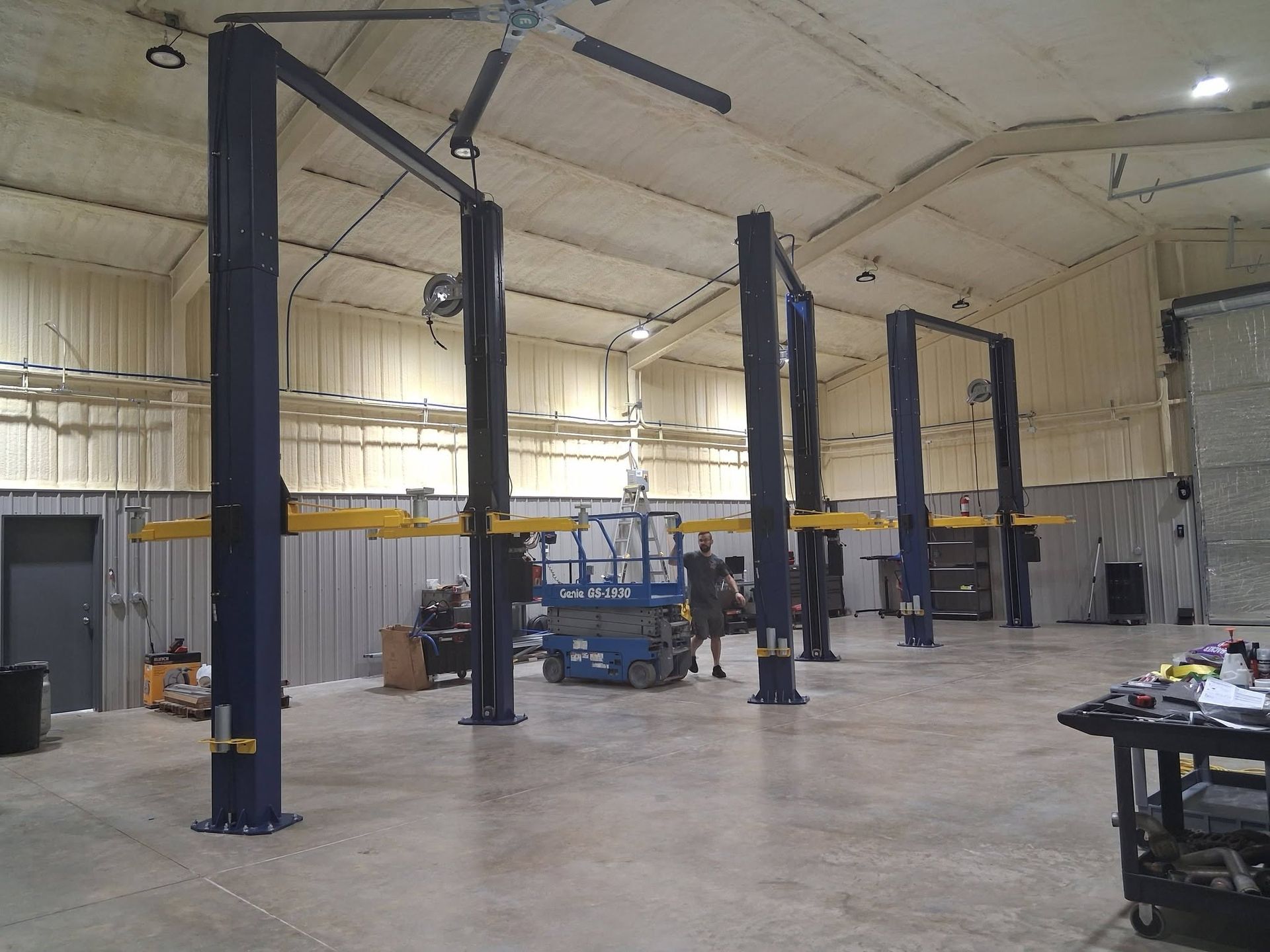 Empty auto shop bay with four dark vehicle lifts in a large industrial warehouse.