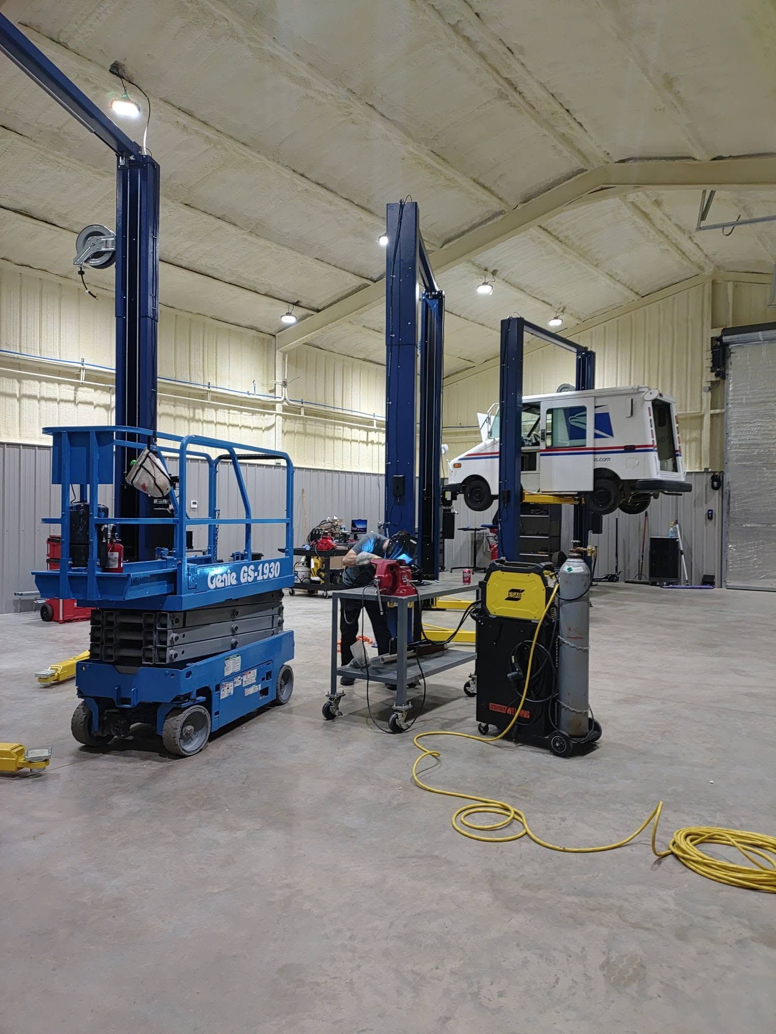 Automotive repair shop with two blue car lifts, tools, and a mechanic working near a vehicle.