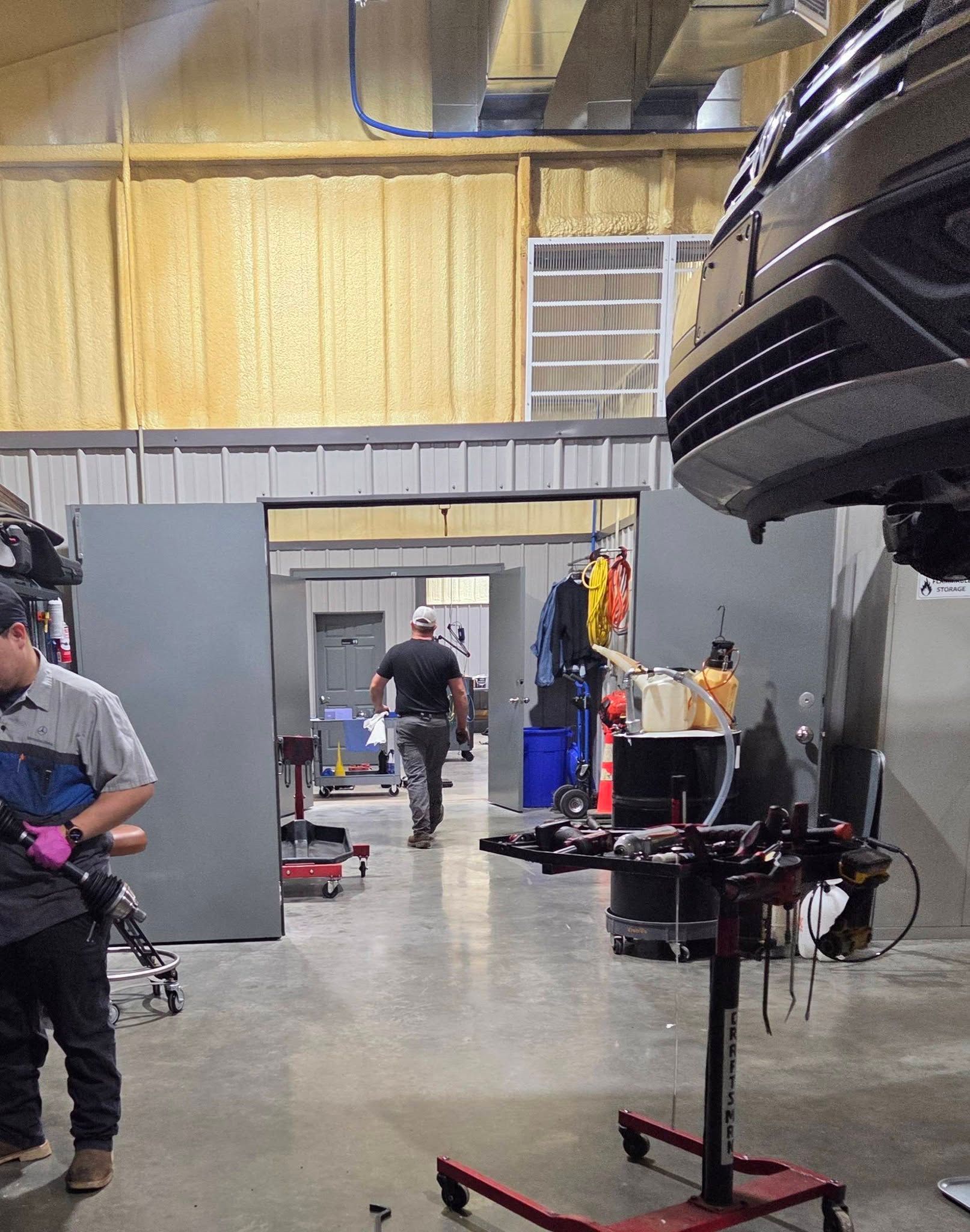 Workshop interior with a person working near a motorcycle lift and another person in the background.