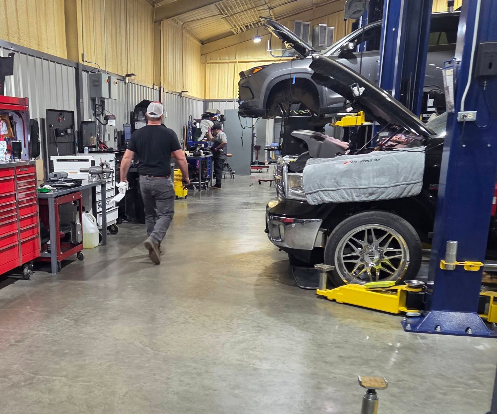 Auto repair shop with a car on a lift and a mechanic walking through the bay.