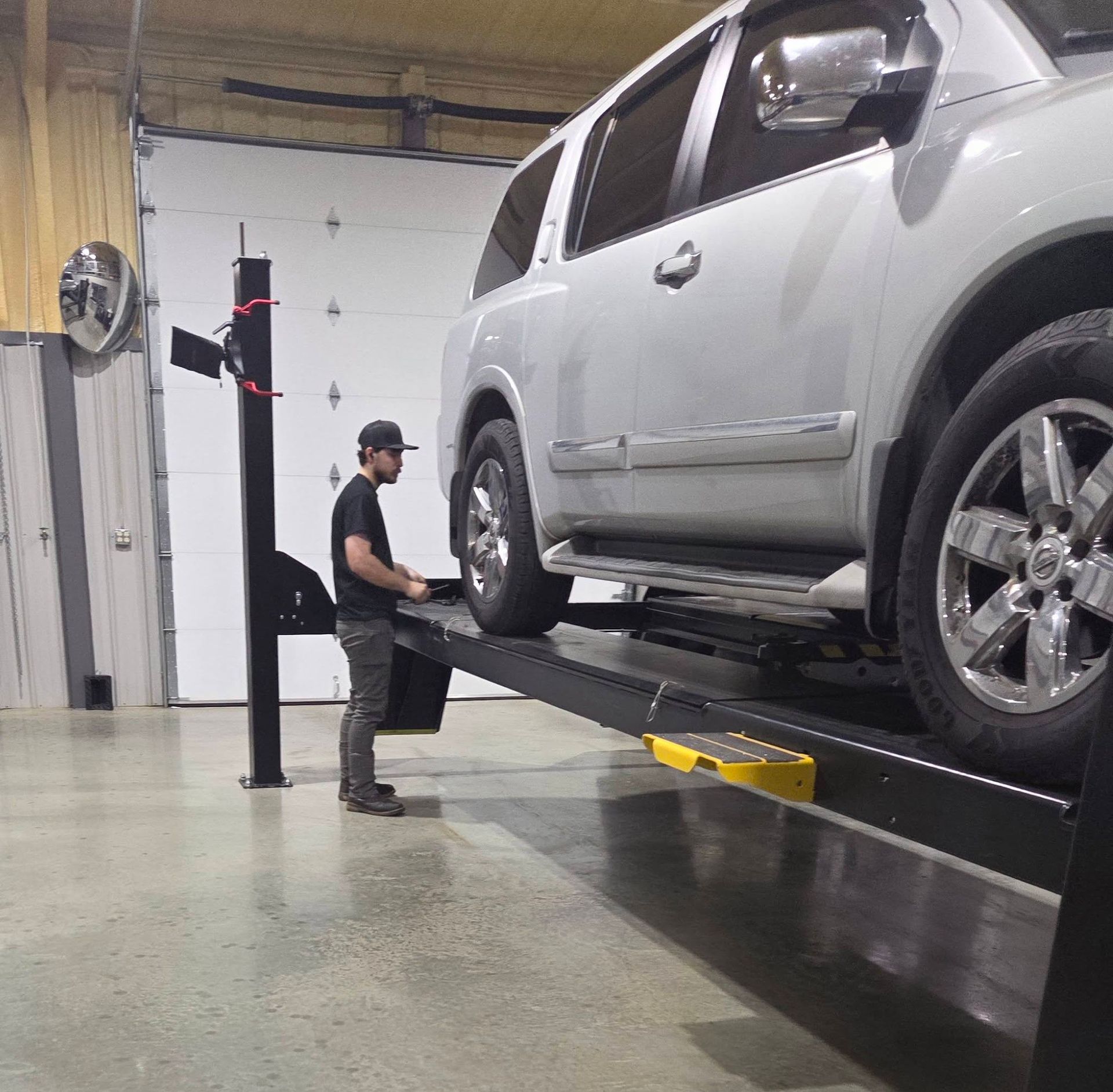 Mechanic working on a silver SUV on a vehicle lift in an auto shop