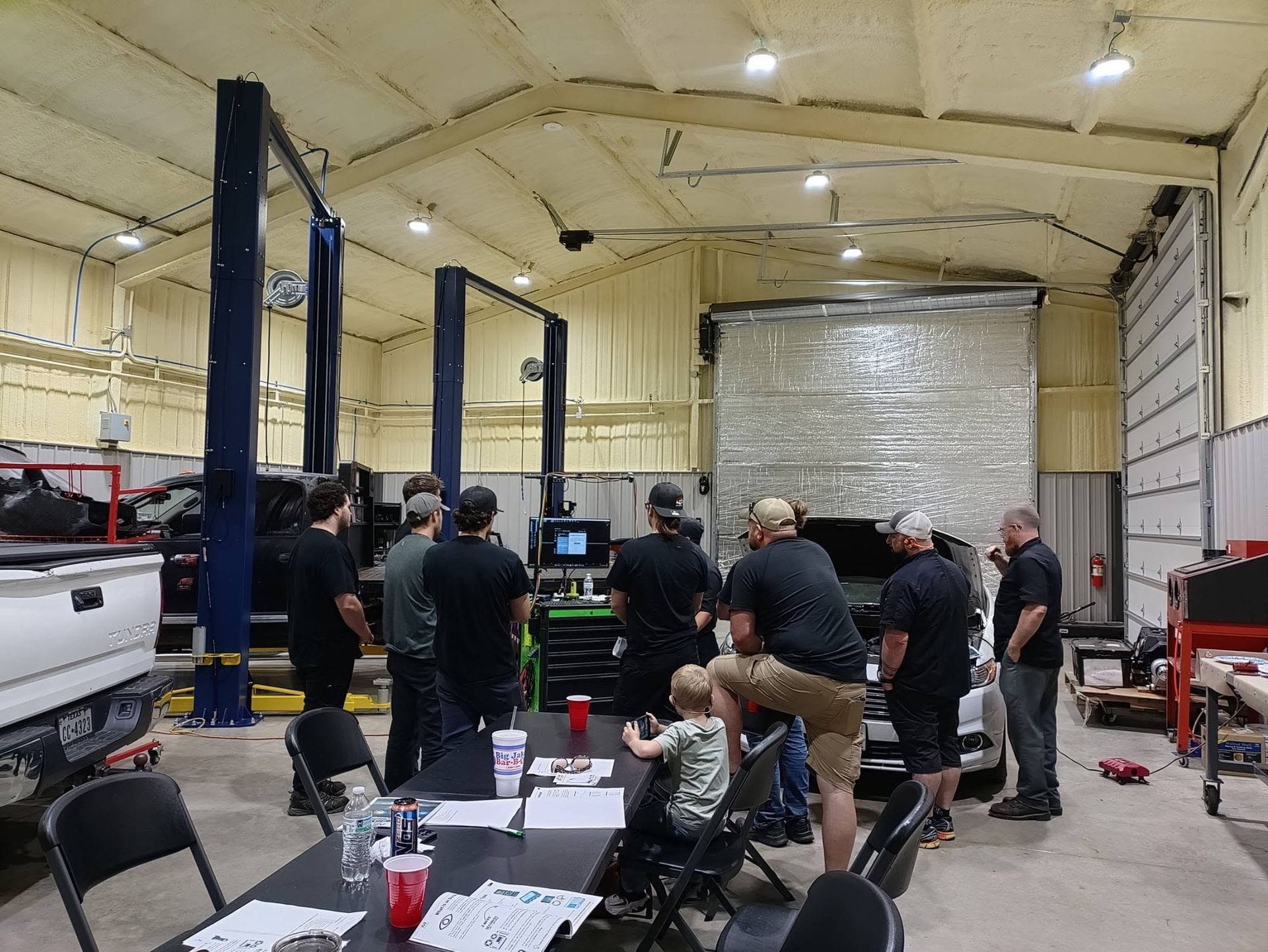 Workshop training session with people gathered around equipment in a large garage bay