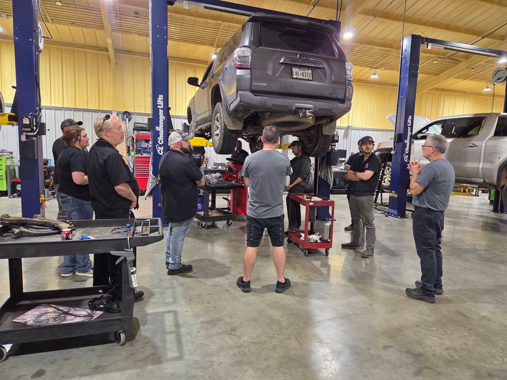 Mechanic shop with a raised SUV and several people gathered around it during vehicle repairs