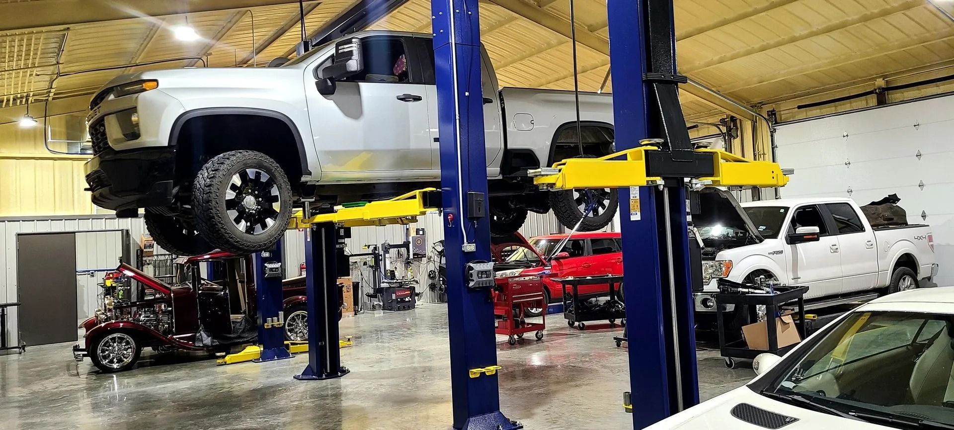 Auto repair shop with vehicles on lifts, including a white truck and red sports cars inside the garage.