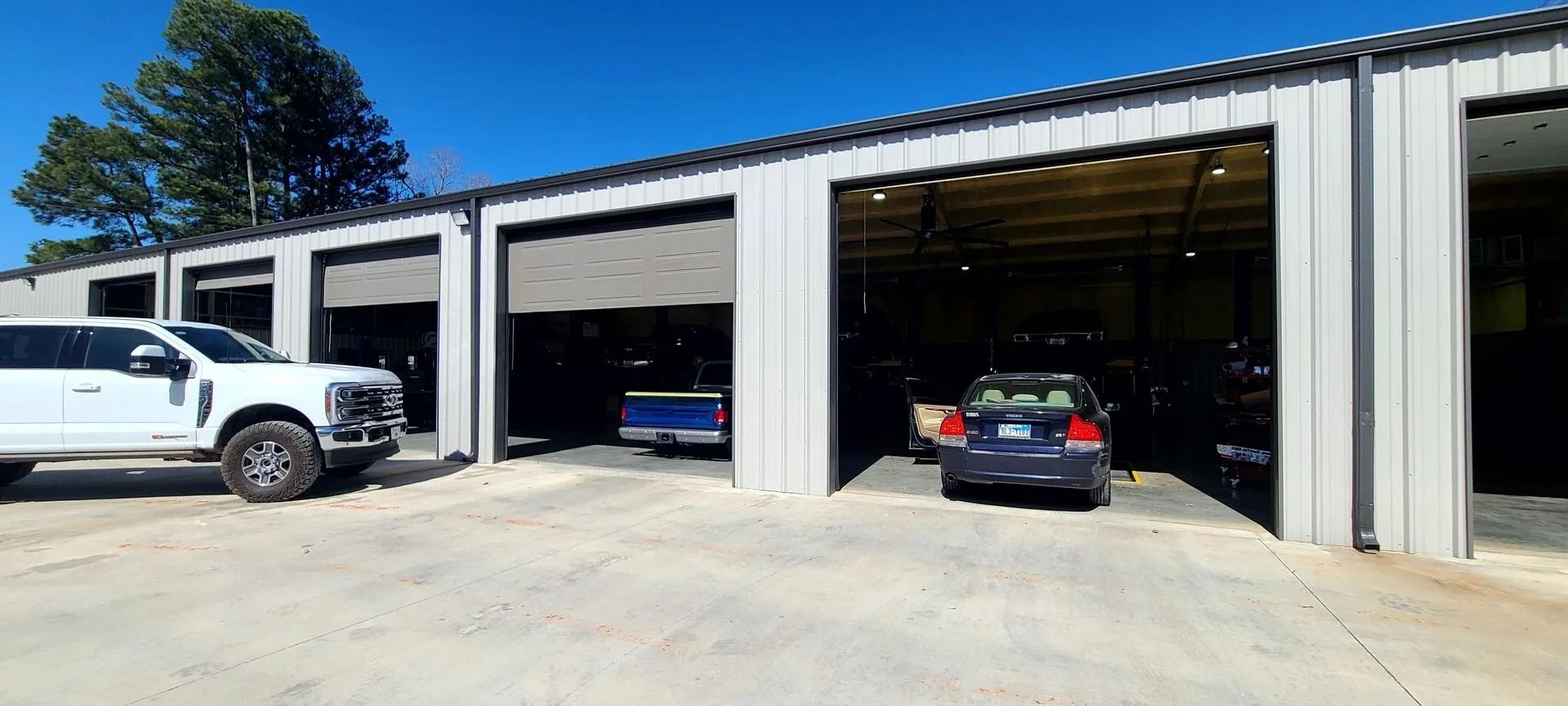 Truck and cars parked outside open garage bays on a sunny day