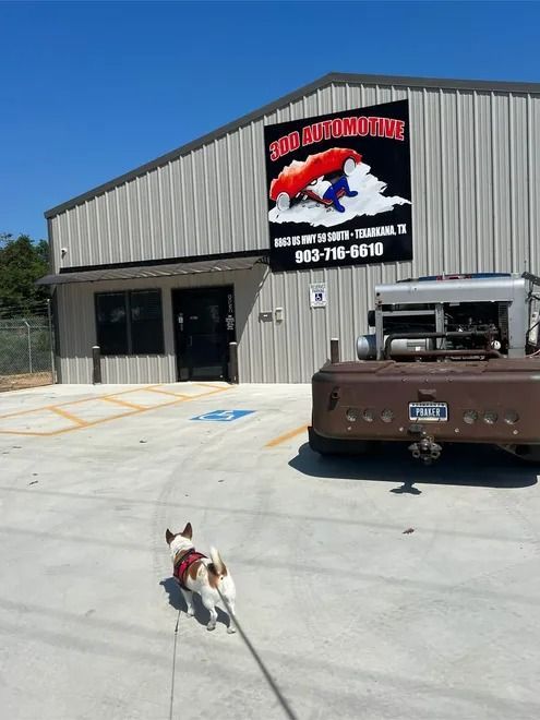 Small dog on leash outside a metal building with a sign and a brown truck parked nearby.