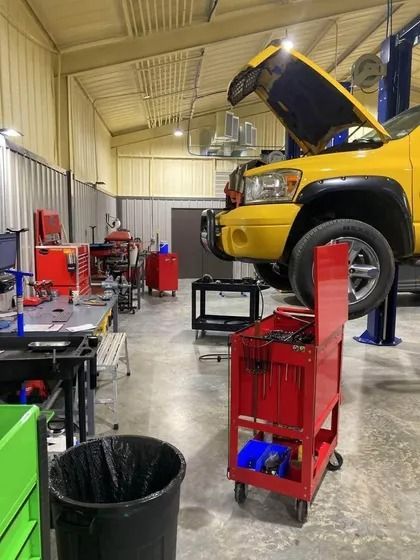 Auto repair shop with a yellow SUV on a lift and tools on carts in a garage bay