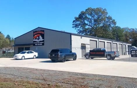 Auto repair shop exterior with parked white, black, and red vehicles on a sunny day