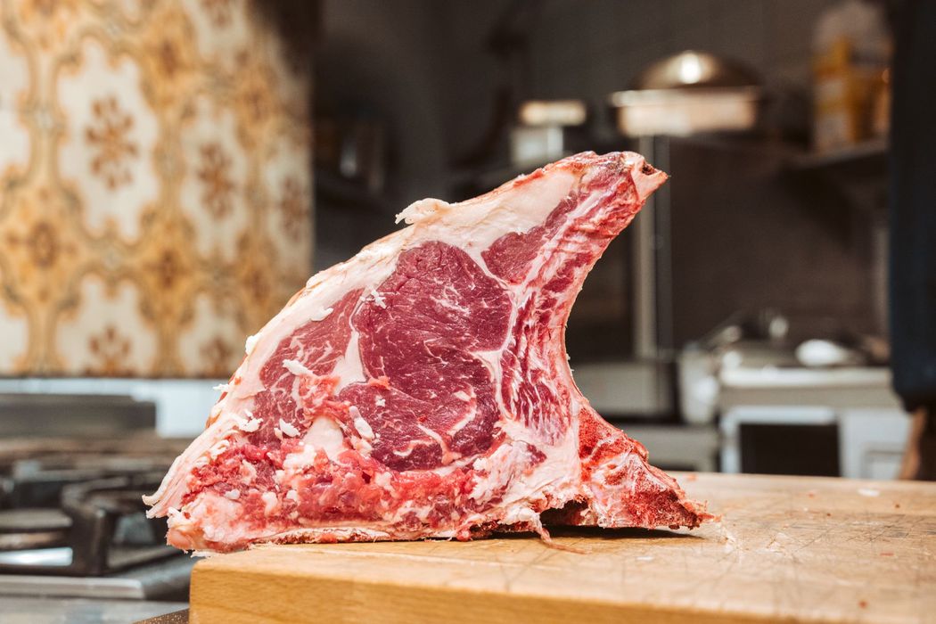 Raw, thick-cut ribeye steak with bone on a wooden cutting board in a kitchen.