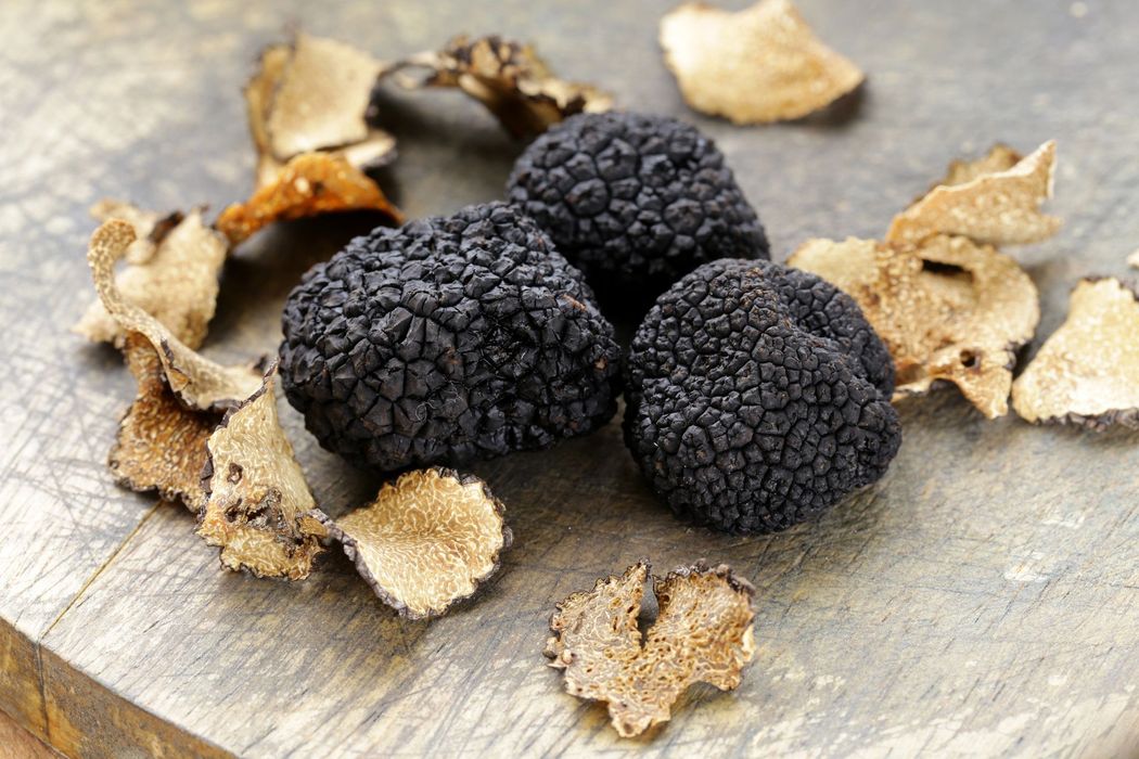 Black truffles and truffle slices on a rustic wooden surface.