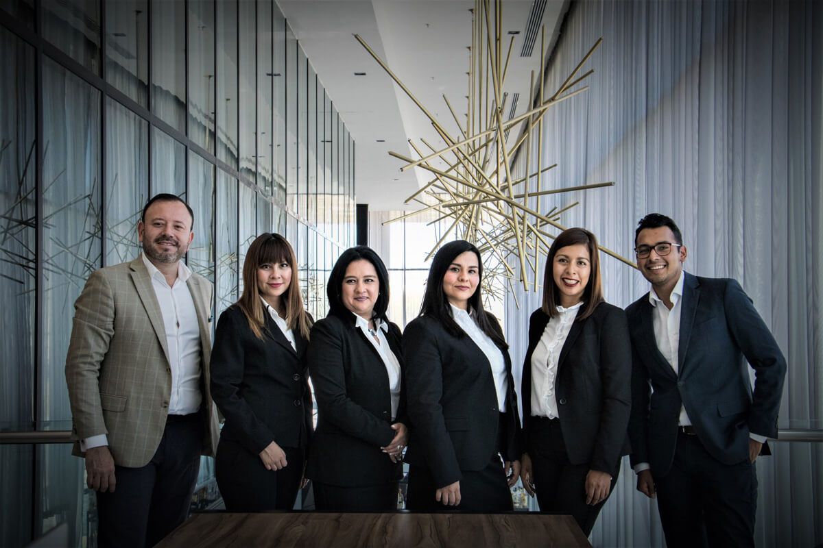 Un groupe de six personnes en tenue de travail, côte à côte dans un bureau moderne avec de grandes fenêtres.
