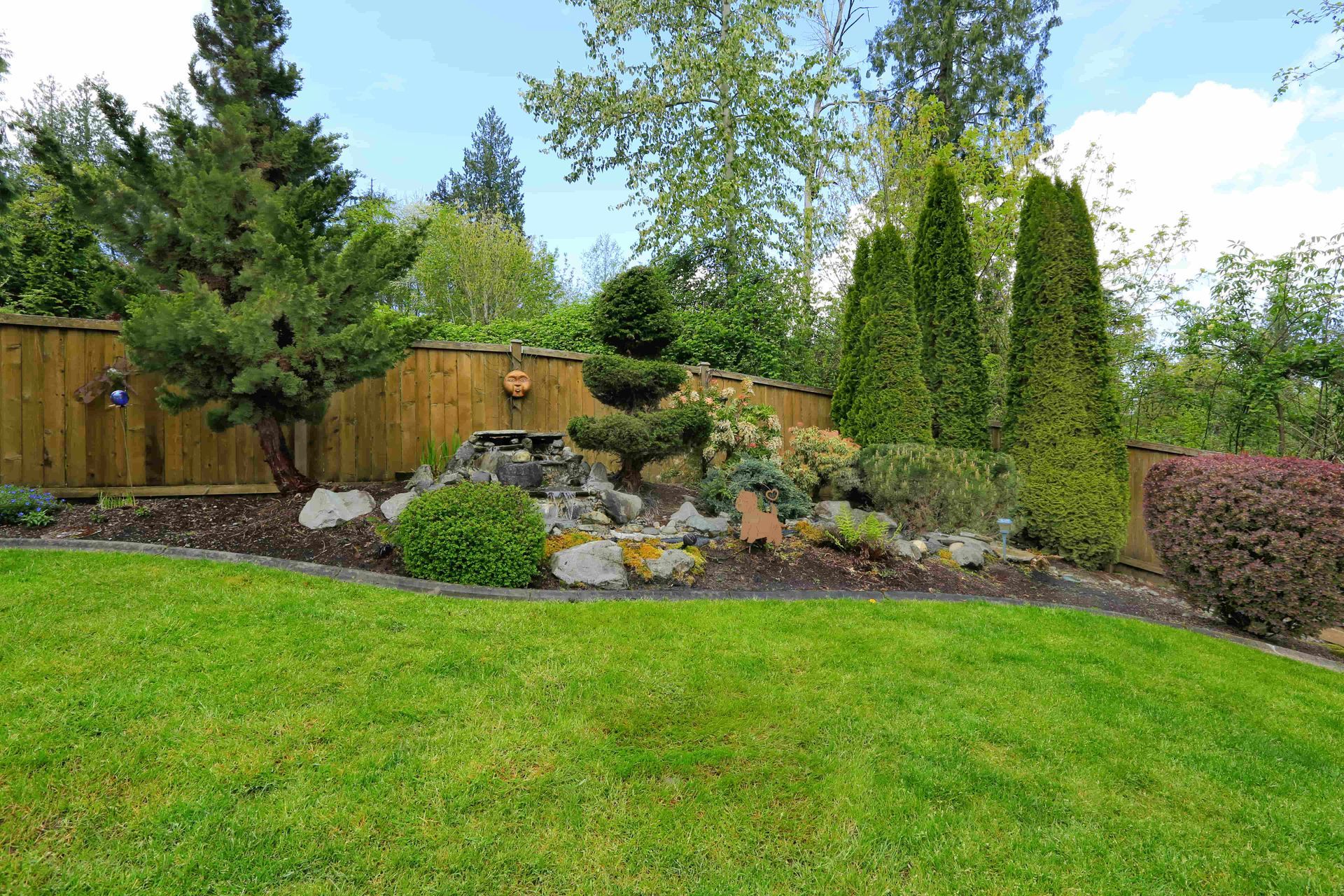 A lush green lawn with a wooden fence and trees in the background.