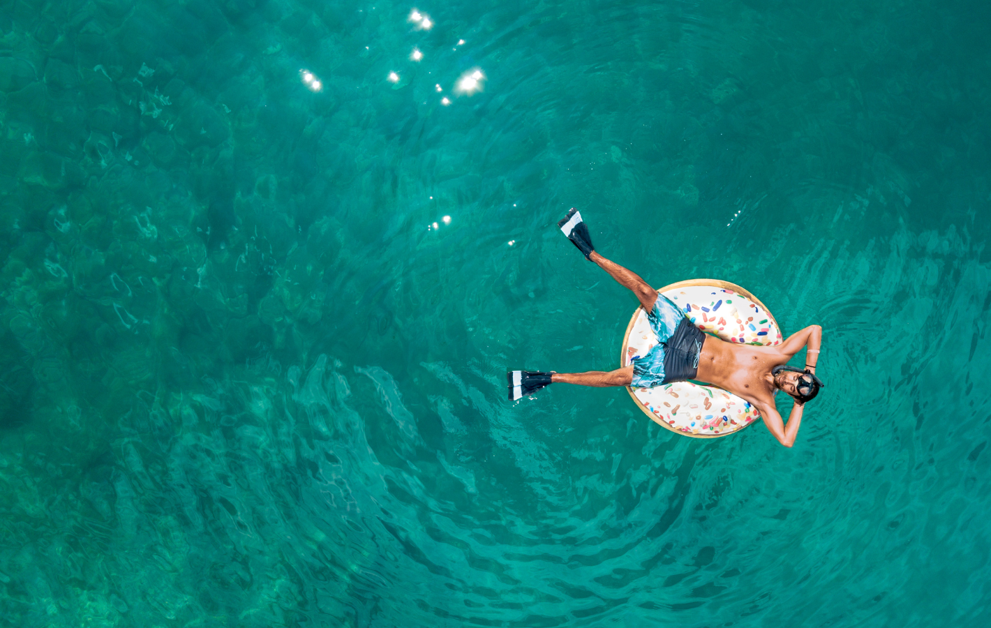 Man floating on a donut-shaped float in turquoise water