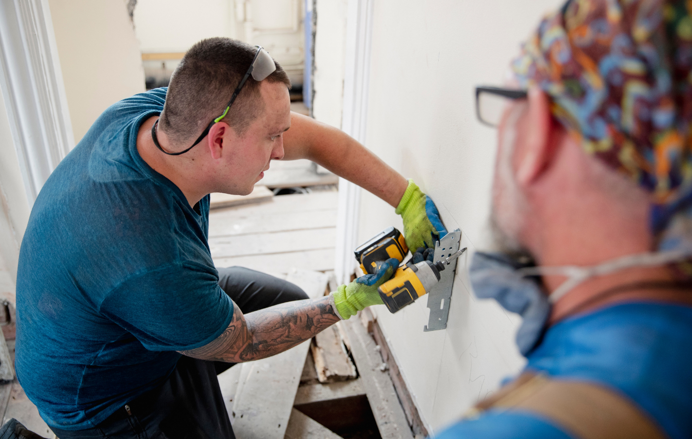 Two men working on construction: one uses a saw on a wall, the other looks on.