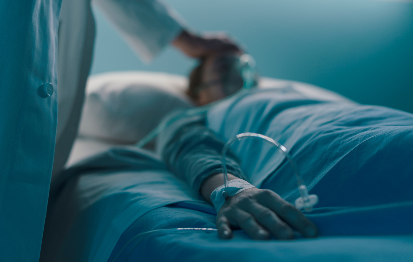 Patient in bed with IV drip; doctor touches head. Blue-toned hospital room.