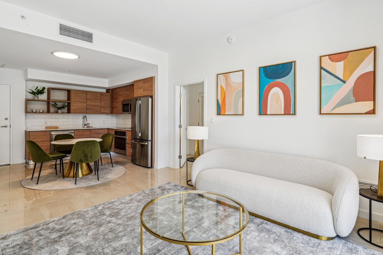 Open-concept living area with a cream sofa, round glass coffee table, dining chairs, and a modern kitchen.