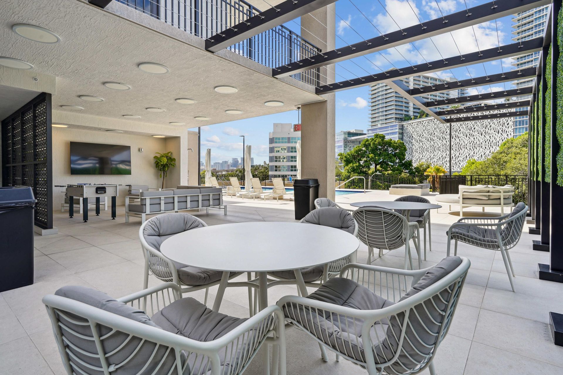 Outdoor rooftop communal lounge with round tables, cushioned chairs, and pool in a city setting.