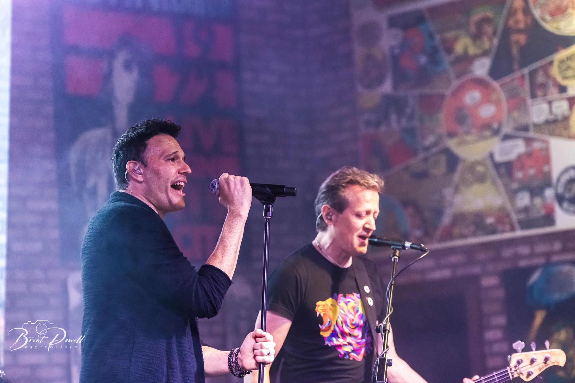 Two men are singing into microphones on a stage.
