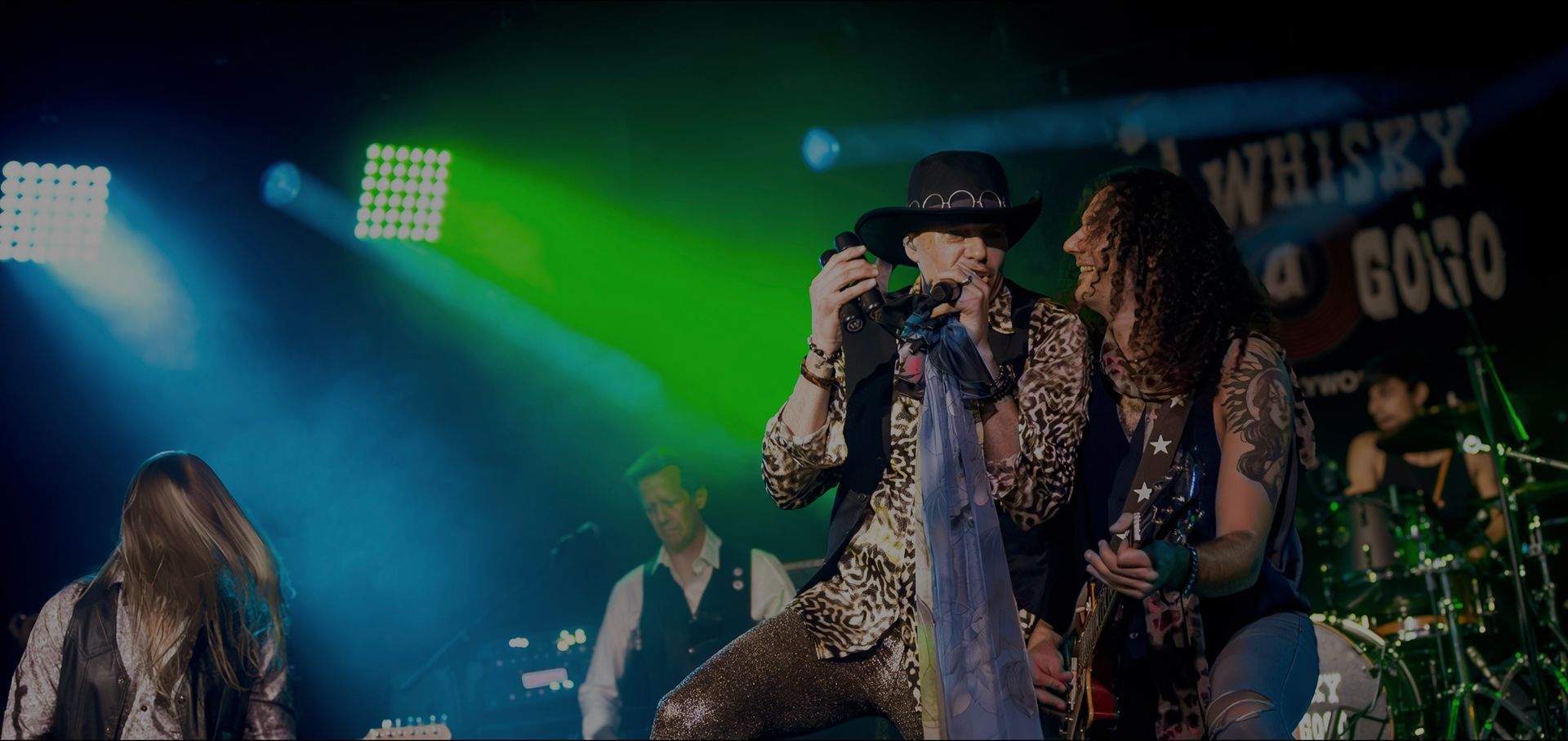 Singer performing on a dimly lit stage with green and blue spotlights, microphone in hand.