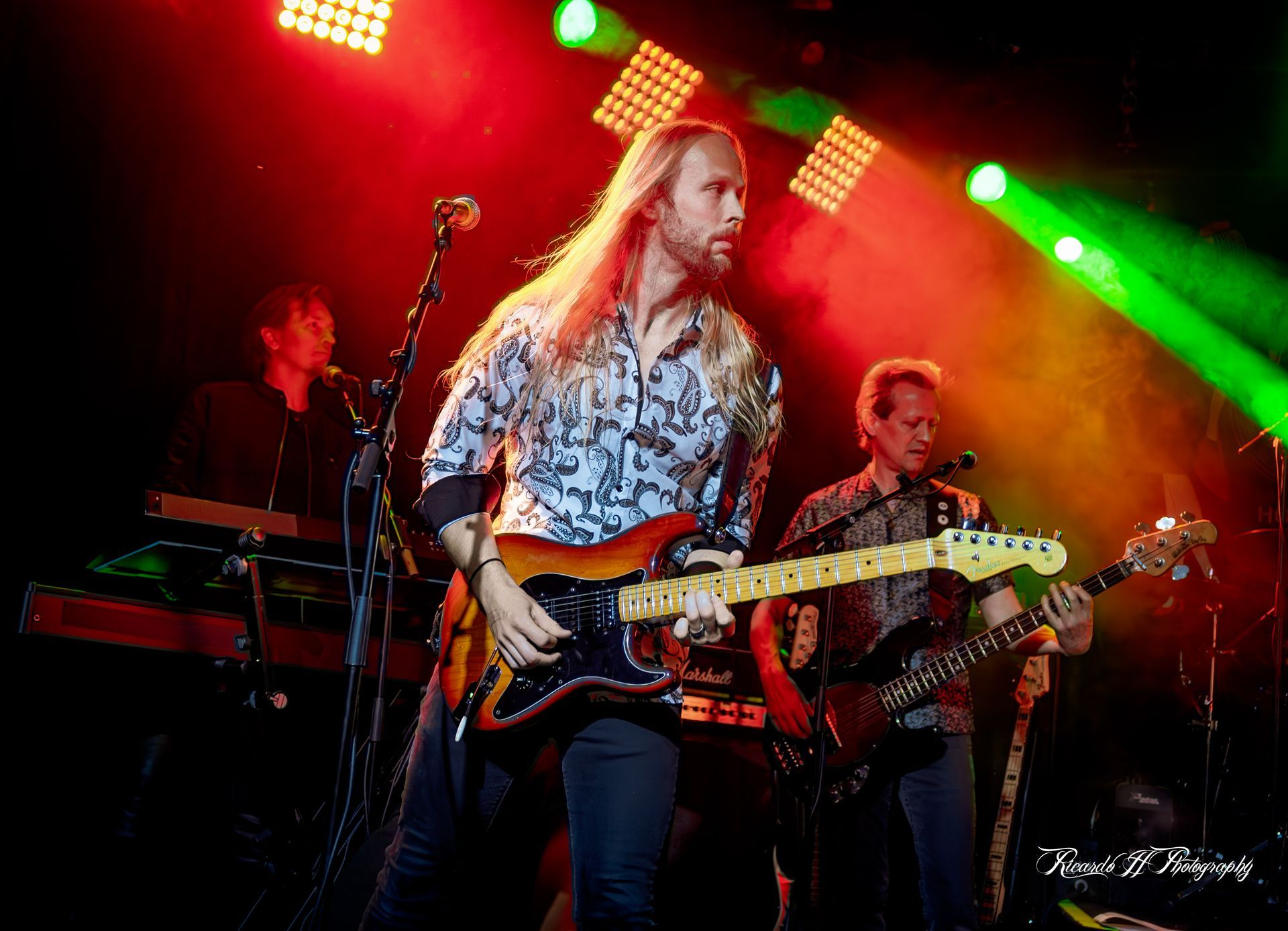 A man with long hair is playing a guitar on a stage.