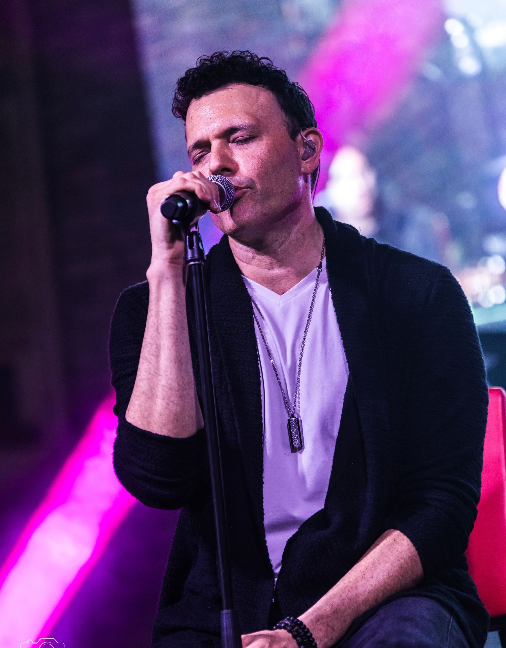A man is singing into a microphone while sitting on a red chair.