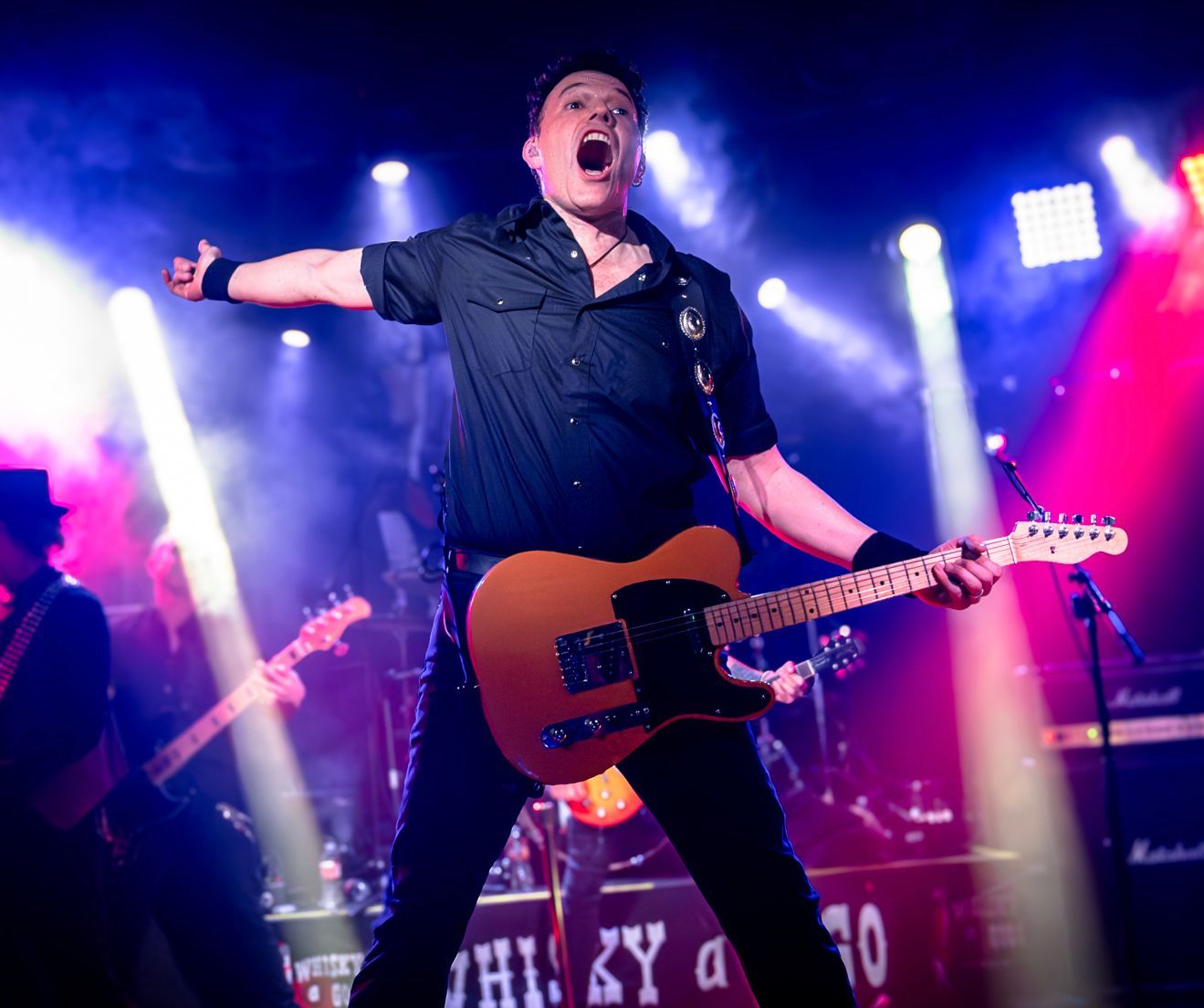 A man singing into a microphone in front of a blackstar amplifier