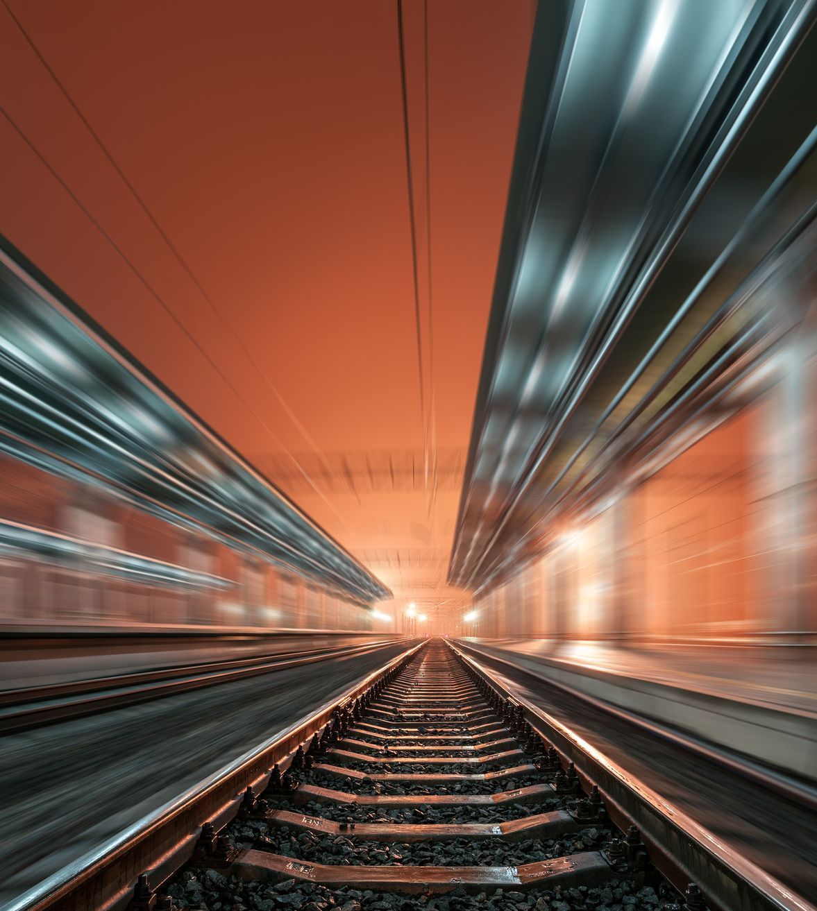 Railroad tracks disappearing into an orange lit tunnel with metallic ceilings.