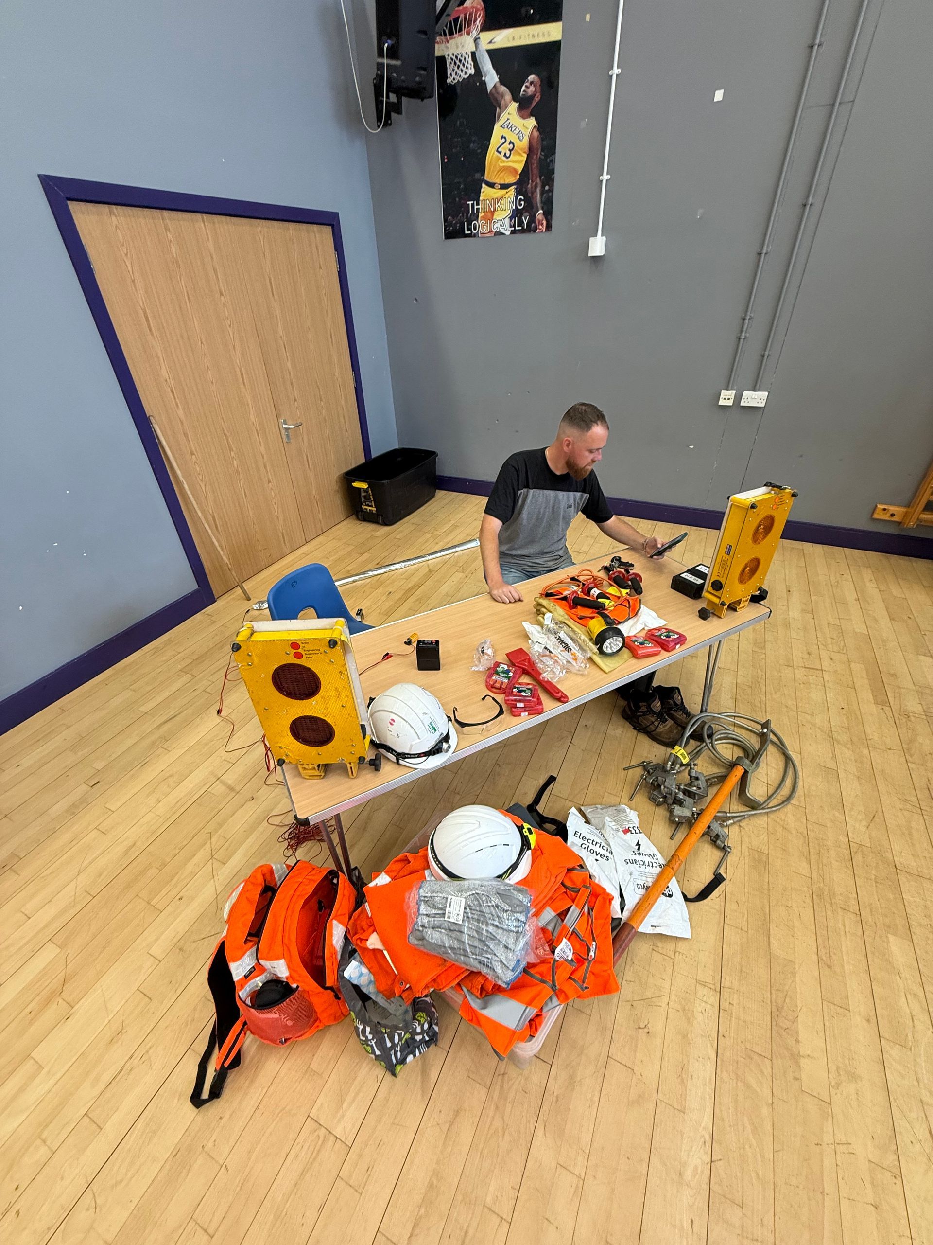 Man at a workbench with safety equipment in a room with a basketball poster.