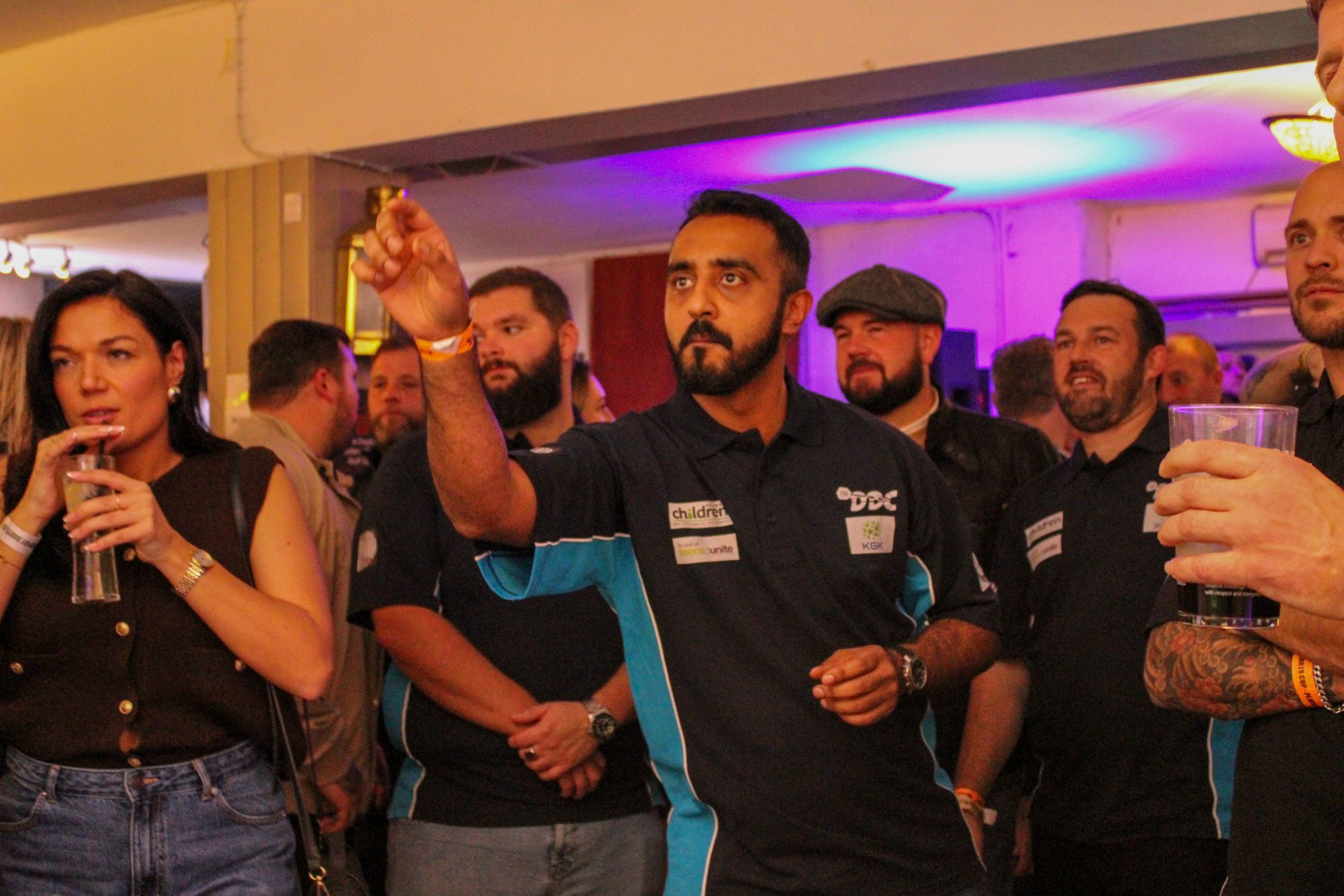 Man throwing a dart in a crowded room, with spectators.